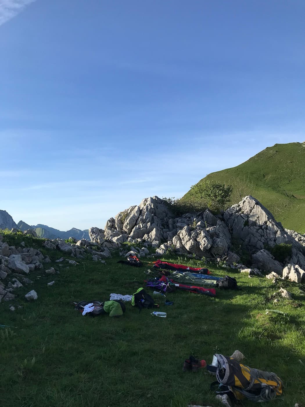 Bivouac installé sur une crête herbeuse en montagne, sacs et matelas au sol face aux sommets